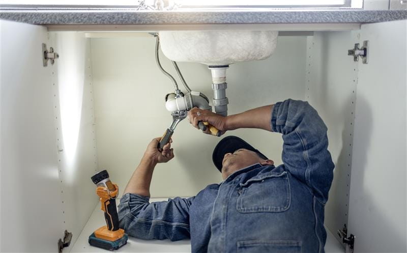 Plumber repairing pipes beneath a bathroom sink in Seal Beach